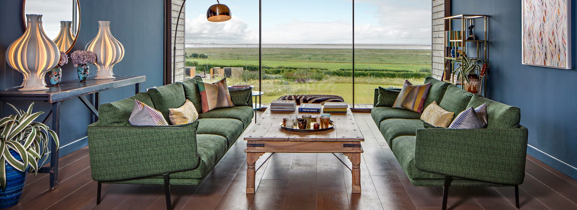 Expansive living room with theEDGE2 glass sliding doors opening onto rolling Norfolk countryside views, green upholstered seating, wooden flooring.