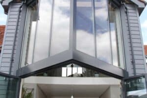 A modern house featuring large, triangular glass windows, an open kitchen, and patio doors, complemented by an elegant extension with a glass roof.