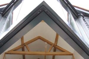 Upward view of a modern building featuring a triangular glass facade, exposed wooden beams, and an elegant extension with a glass roof.