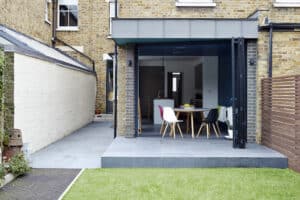 A modern patio view of a stunning bifold doors extension features a dining table and chairs, seamlessly leading to an open kitchen.
