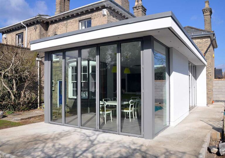 A sleek, flat roof extension with an overhang complements the older brick house, boasting large sliding doors that open to a stylish dining area.