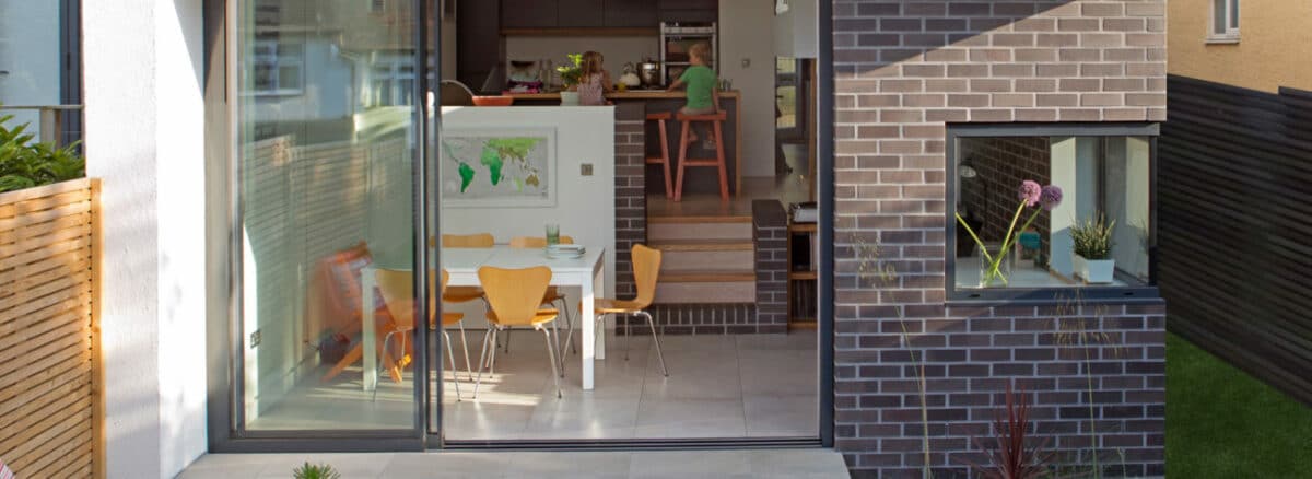 theEDGE2 glass sliding door opens modern kitchen to bright patio with dining area, maximising light and seamless indoor-outdoor living.