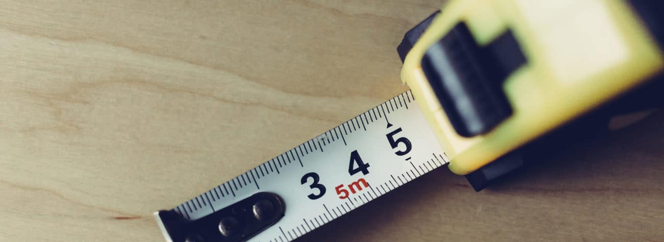 A close-up of a measuring tape extended to 5 meters, placed on a wooden surface.