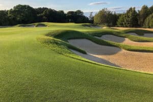 A golf course with well-maintained green fairways and multiple sand bunkers, surrounded by trees.