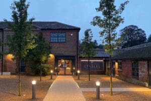 Exterior view of The Stables building at dusk, surrounded by trees and pathway lights.