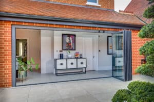 Modern patio with slide and turn doors leading into a room featuring a sideboard with decor, framed art on the walls, and potted plants.