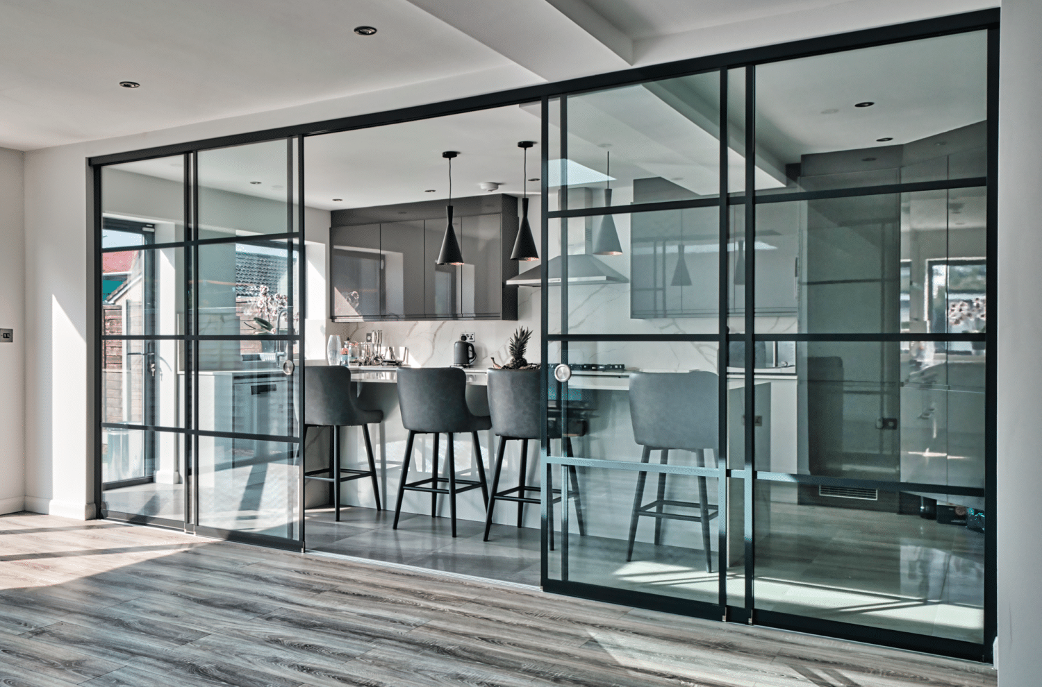 SF22 heritage sliding doors with gridded black frames divide a modern kitchen, featuring pendant lights and bar seating visible through the glass panels.