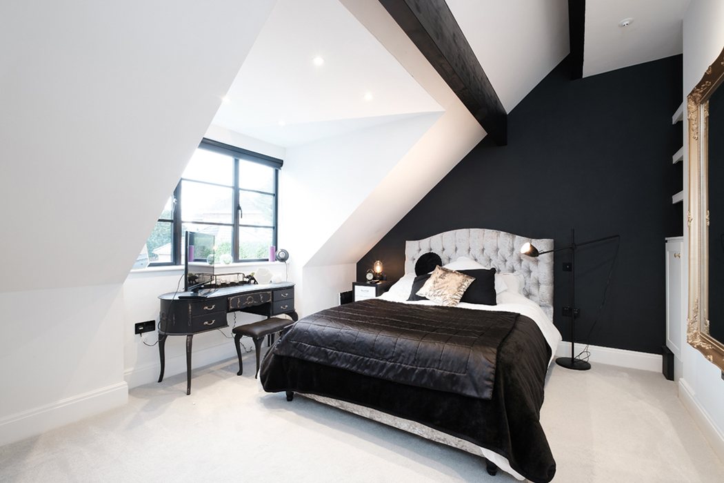 Modern bedroom with angled ceiling, featuring a bed with black and white bedding, a black wall, desk with chair, and a large window.