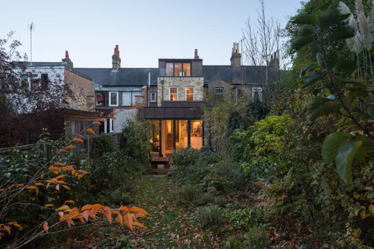 View of a modern house extension with large glass windows, surrounded by a lush garden, in a residential neighborhood.