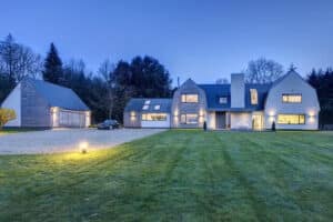 Modern two-story house featuring aluminium casement windows, a spacious driveway, and a detached garage. Surrounded by a well-maintained lawn and trees. Evening lighting creates a serene ambiance.