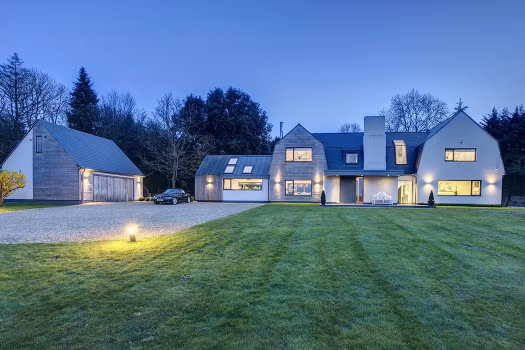 Modern two-story house featuring aluminium casement windows, a spacious driveway, and a detached garage. Surrounded by a well-maintained lawn and trees. Evening lighting creates a serene ambiance.