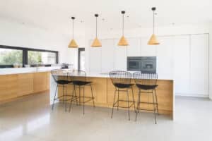 Modern kitchen featuring light wood cabinets, a large island with wire-frame stools, pendant lights, and built-in appliances. Aluminium casement windows allow natural light to flood the space, enhancing its sleek and airy ambiance.