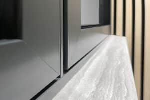 Close-up of a modern window frame and sill featuring sleek black metal, reminiscent of aluminium casement windows, paired with a textured gray stone surface, set against vertical wooden paneling.