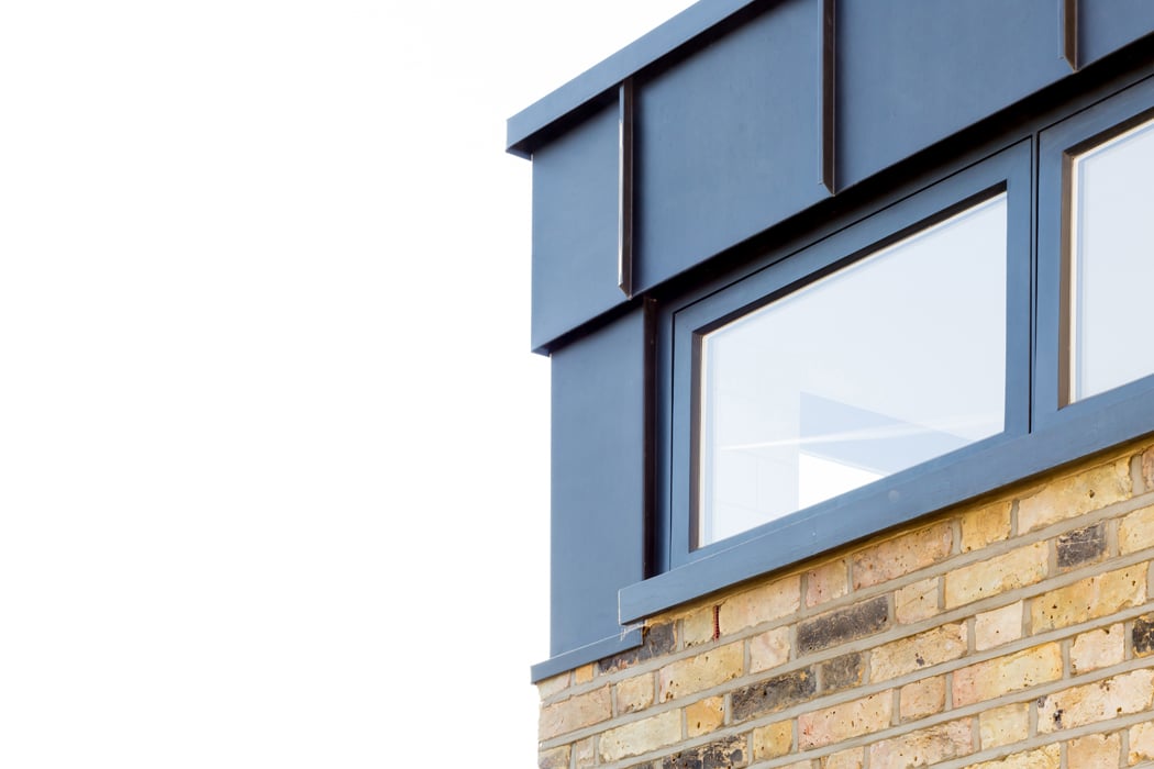 Close-up of a building corner featuring a brick wall and large aluminium casement windows framed in dark material, set against a clear sky.