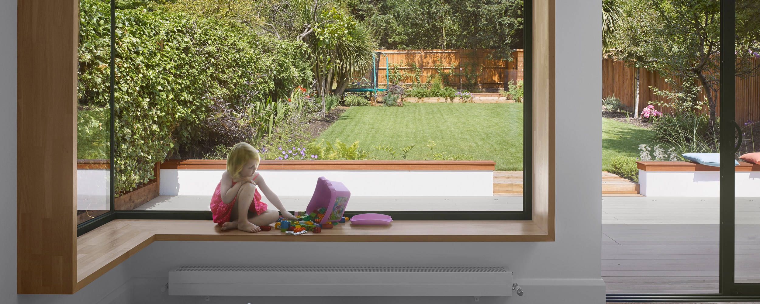 A stylish kitchen extension featuring a frameless glass-to-glass corner window incorporating a window seat for views out into the garden