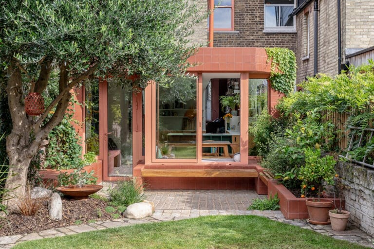 A modern extension with large glass doors and terracotta tiles, surrounded by lush greenery and garden plants.