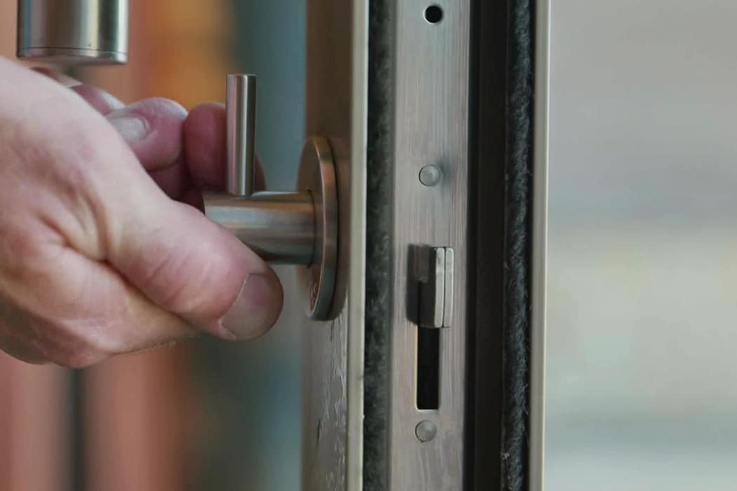 A person’s hand turns a modern metallic door handle, showing the lock mechanism on the door edge.