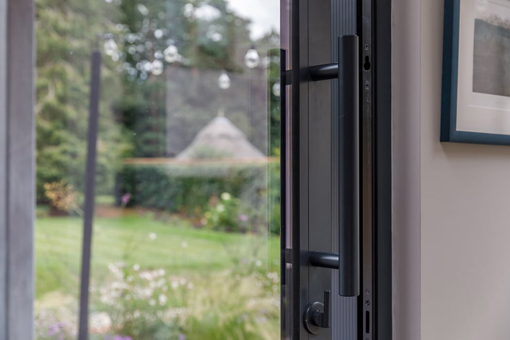 A close-up of a partially open glass door, with a view of a green garden and trees outside.