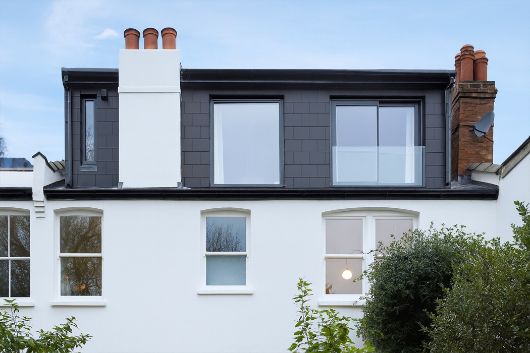 Modern white house with sleek glass Juliet balcony and frameless glass balustrade on upper storey extension.