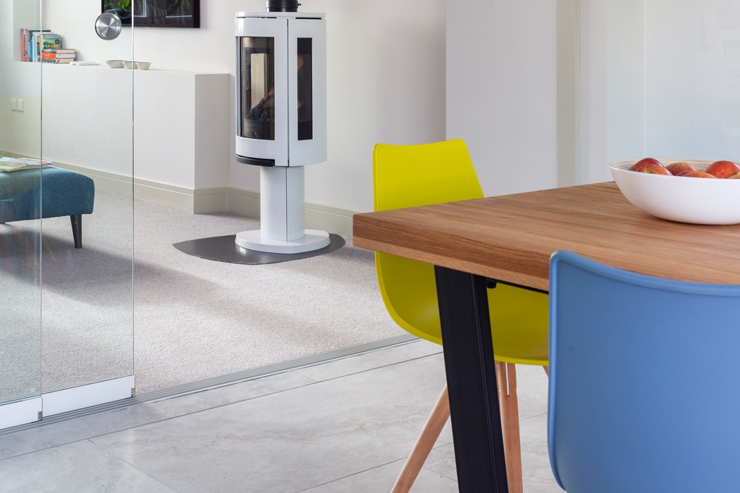 Modern kitchen with SF20 frameless glass sliding door separating dining area, featuring colourful chairs and wooden table.