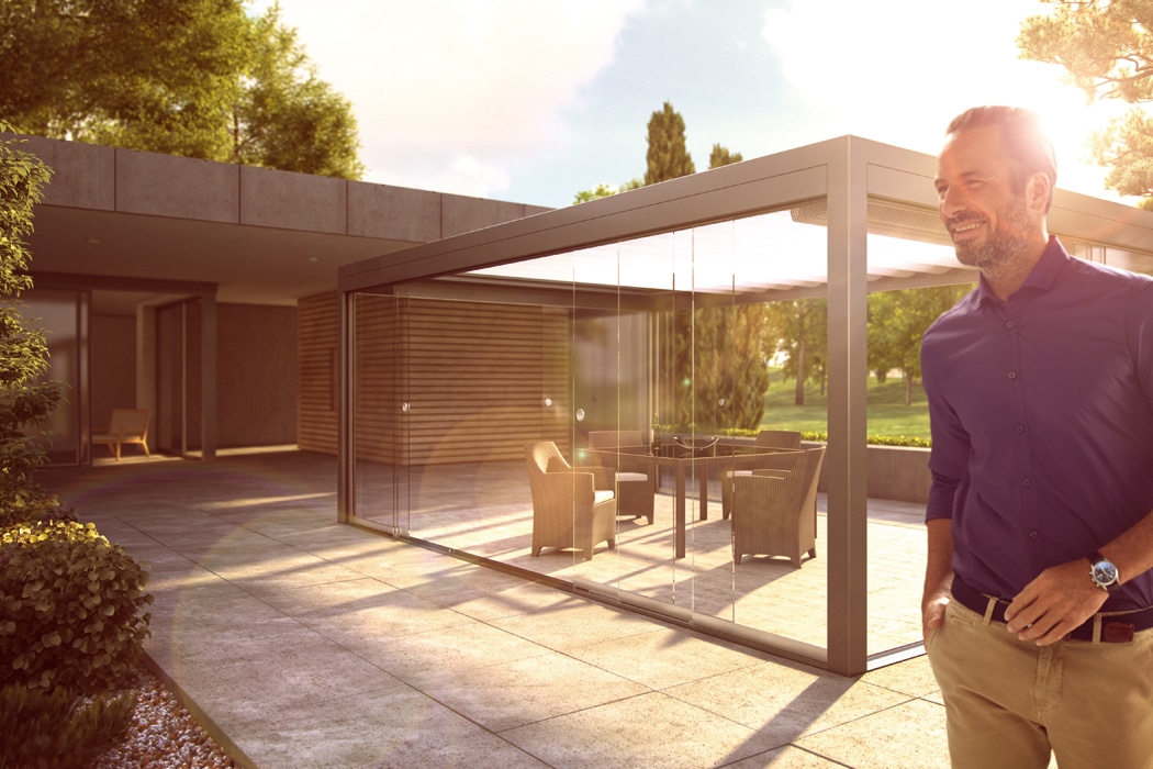 Man admiring frameless glass SF20 single sliding door opening onto modern patio with contemporary pergola and garden views.