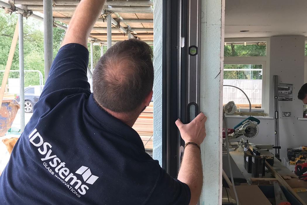 A person in an IDSystems shirt uses a spirit level to check the alignment of a door frame at a construction site.