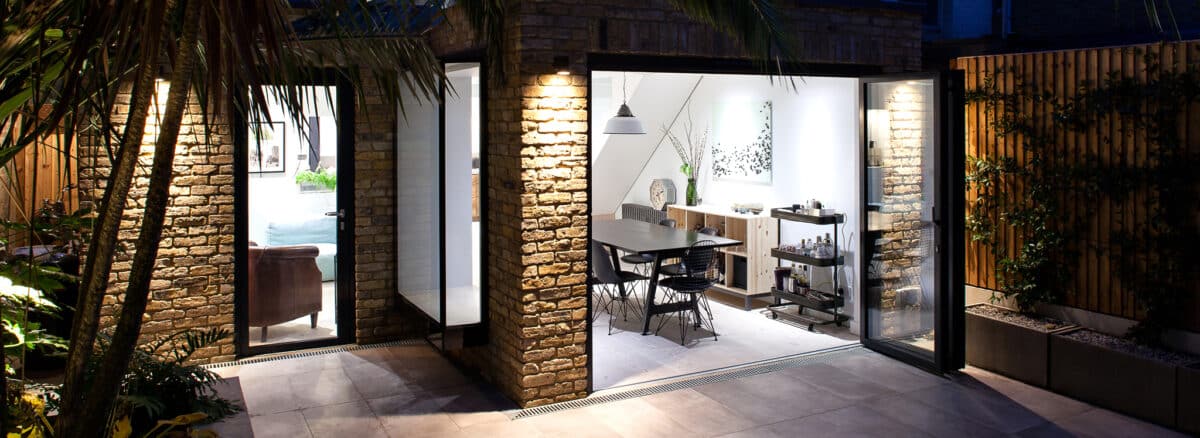 Modern West London bifold extension by Maxwell and Company featuring floor-to-ceiling glazing, creating a seamless transition between outdoor courtyard and bright interior dining space.