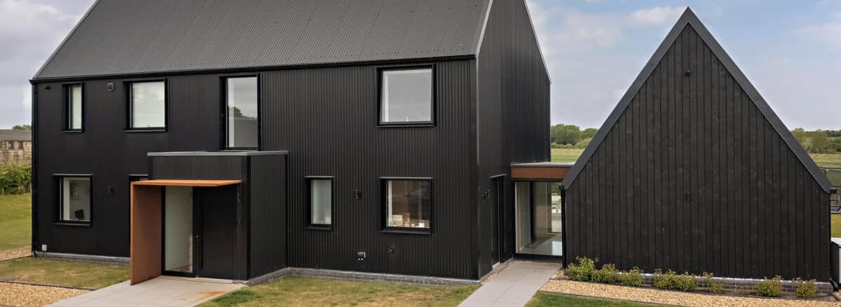 Modern black barn conversion featuring extensive glazing systems, bifold doors, and large windows creating contemporary living spaces in rural setting.