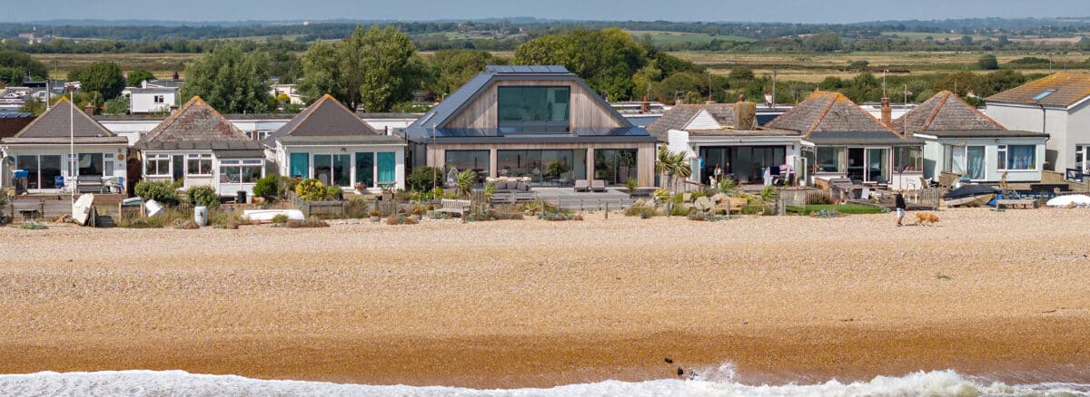 Modern beachfront home featuring expansive glazing and bifold doors overlooking Pevensey Bay beach and Sussex coastline.