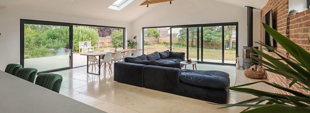 Modern open-plan living space with black aluminium bifold doors opening onto a garden, featuring contemporary furnishings and natural light.