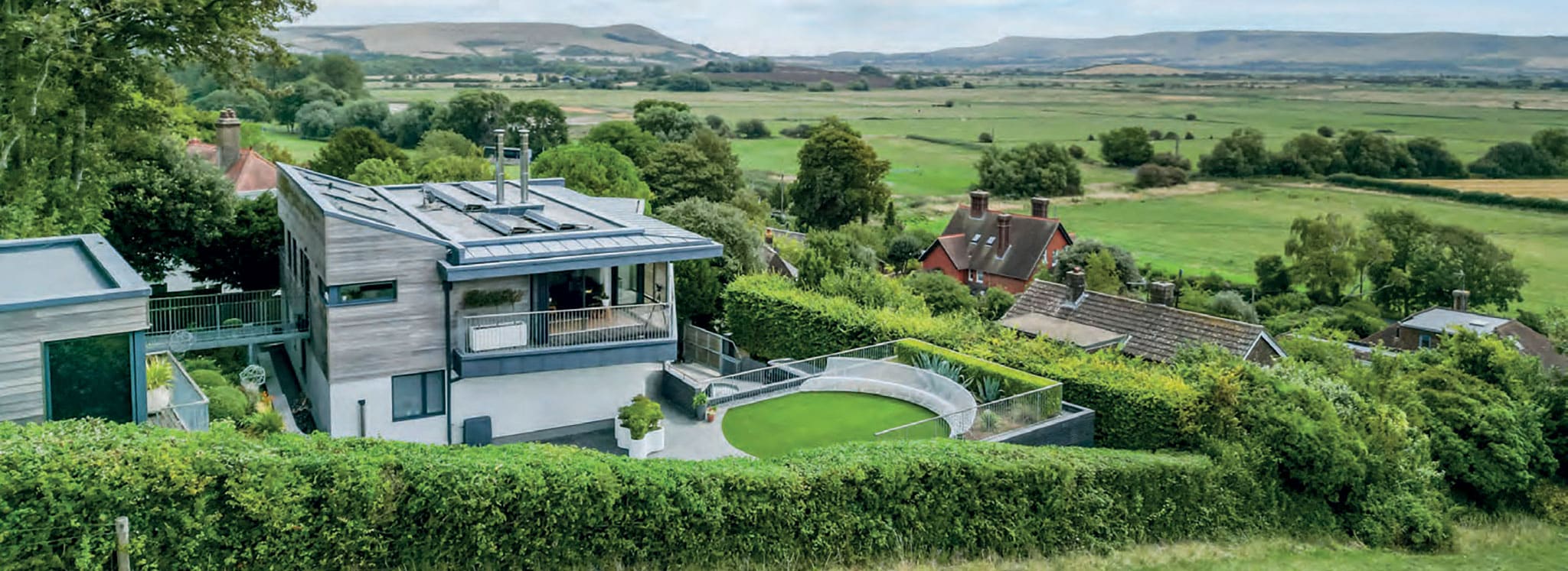 Contemporary hilltop home featuring expansive glazing and sliding doors overlooking rolling countryside valleys and distant hills.