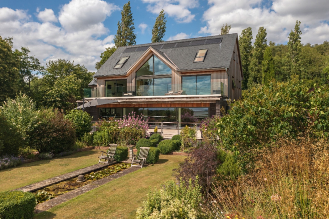 Contemporary riverside home featuring expansive 4 panel sliding glass doors opening onto manicured gardens with seating area