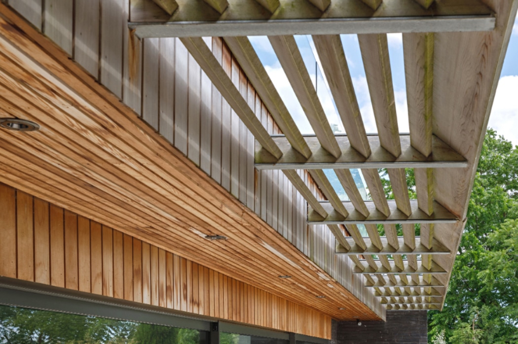 Modern riverside home with timber cladding and wooden pergola structure providing filtered natural light