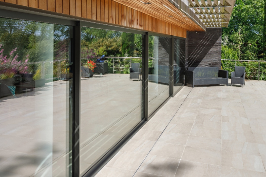 Four-panel sliding glass door opening onto a contemporary riverside terrace with paving and garden views