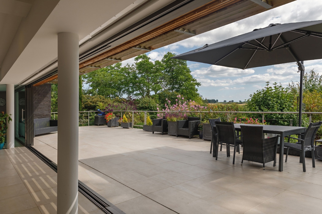 Contemporary riverside home with expansive 4 panel sliding glass doors opening onto a spacious terrace overlooking gardens and countryside.