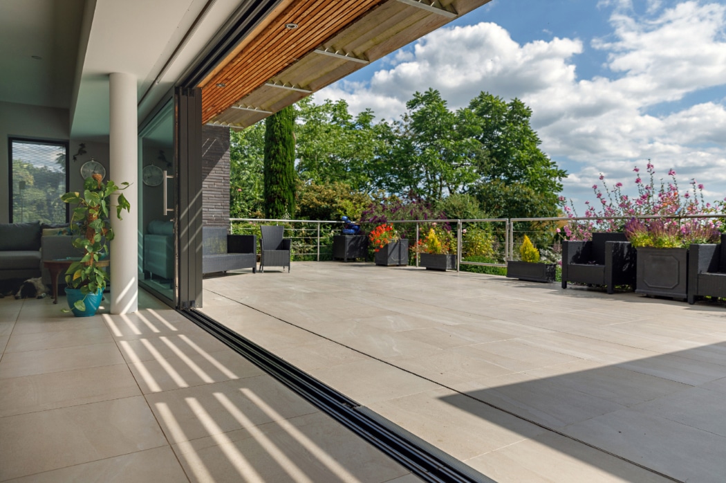 Modern 4 panel sliding glass door opens onto a riverside terrace with planters and countryside views