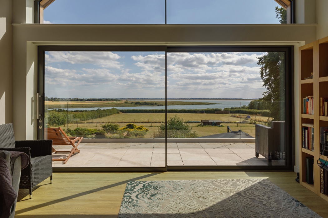 Four-panel sliding glass doors open to a sunny terrace overlooking Essex marshland and water.