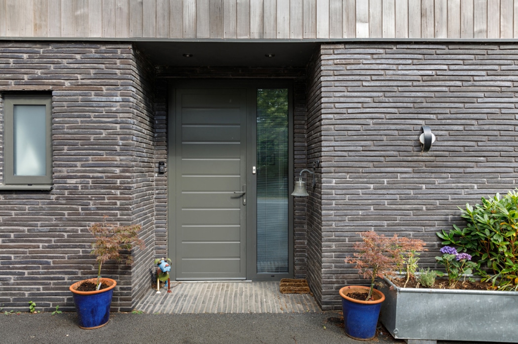 Contemporary riverside home entrance featuring a sleek grey sliding glass door with sidelights and brick facade