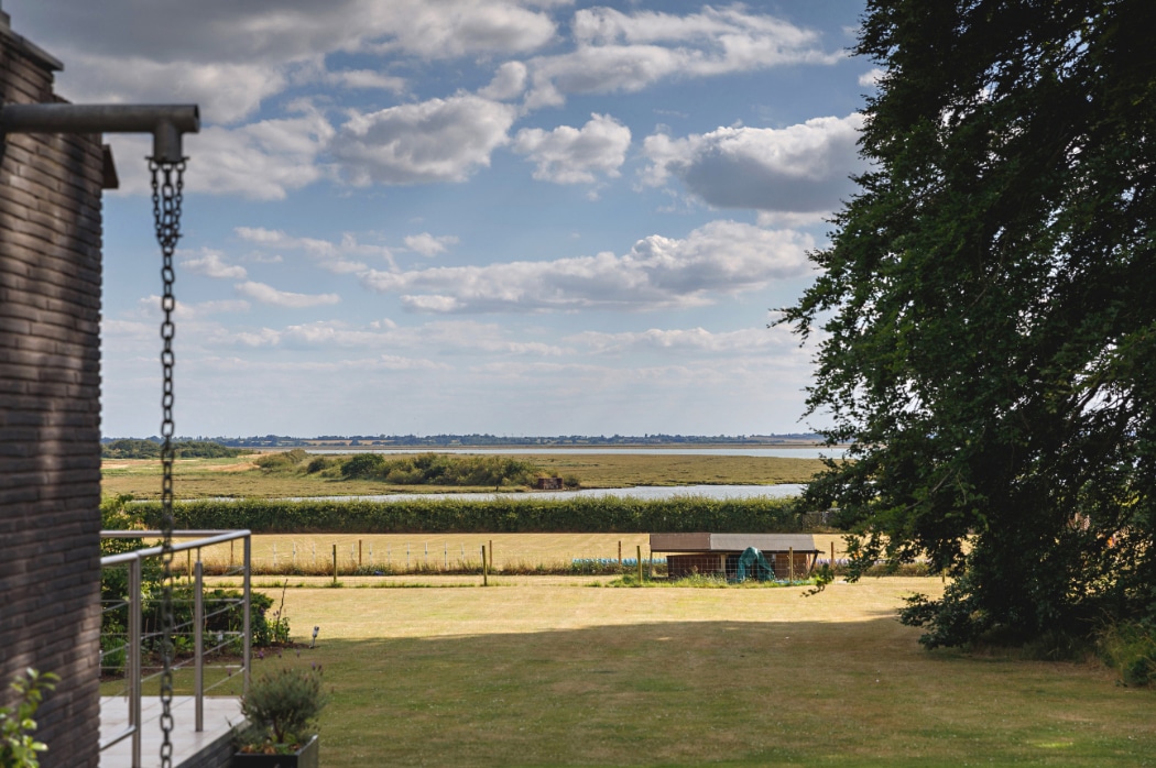 Contemporary riverside Essex home with expansive 4 panel sliding glass doors opening to manicured gardens and water views beyond.