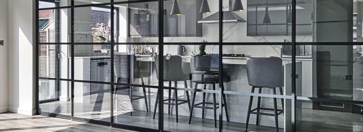 Contemporary open-plan kitchen and dining space separated by sleek black SF22 sliding glass partitions, maximising light and versatility.