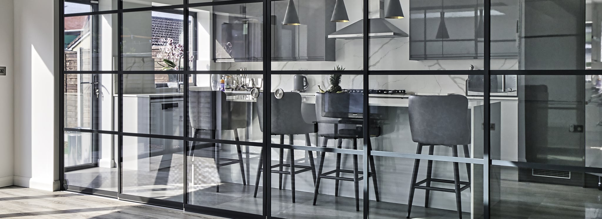 Contemporary open-plan kitchen and dining space separated by sleek black SF22 sliding glass partitions, maximising light and versatility.
