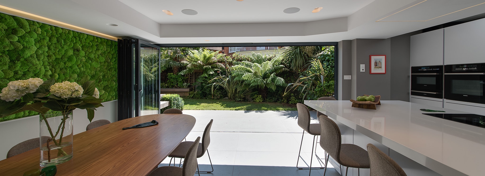 Modern kitchen with seamless bifold doors opening onto lush garden, featuring slim-profile aluminium frames and unobstructed views.