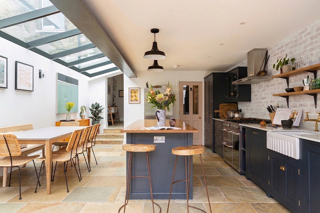 Modern kitchen with lean glass roof flooding natural light, featuring bespoke glazing and black cabinetry with wooden accents.