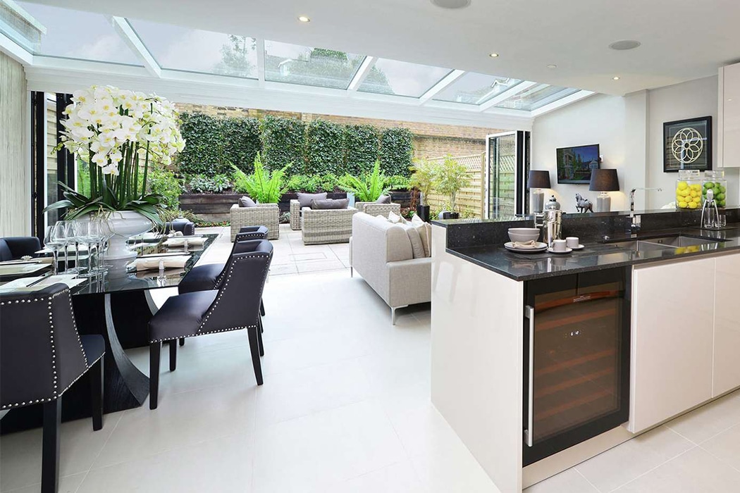 Modern open-plan kitchen and living space flooded with natural light from structural glass roof, featuring slim-profile aluminium frames and seamless garden views.