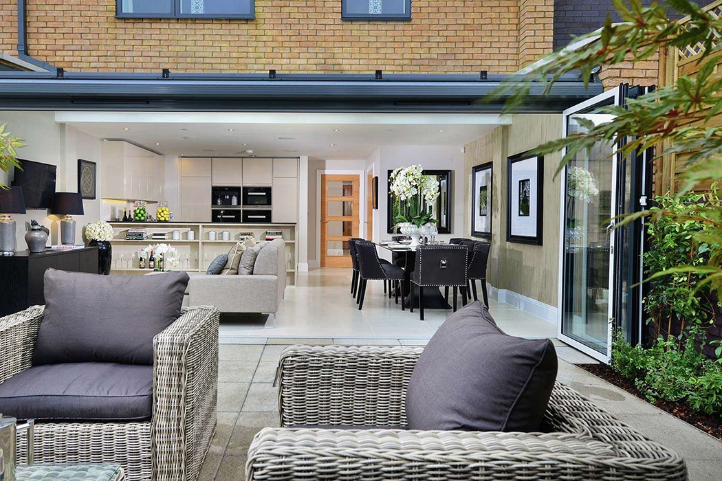 Contemporary open-plan living space featuring structural glass roof extending into garden, with sliding doors and bespoke glazing maximising natural light and views.