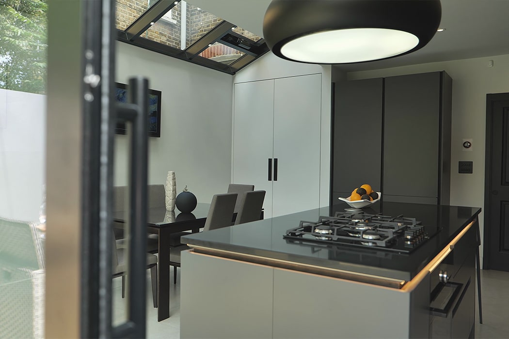 Modern kitchen with structural glass roof flooding space with natural light, featuring bespoke glazing and sleek aluminium framing.