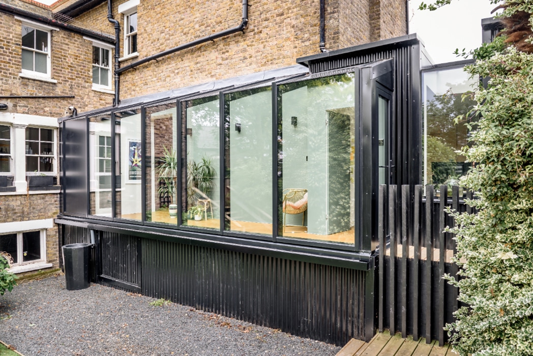 Modern black aluminium glass roof extension with sliding doors overlooking a contemporary garden courtyard.