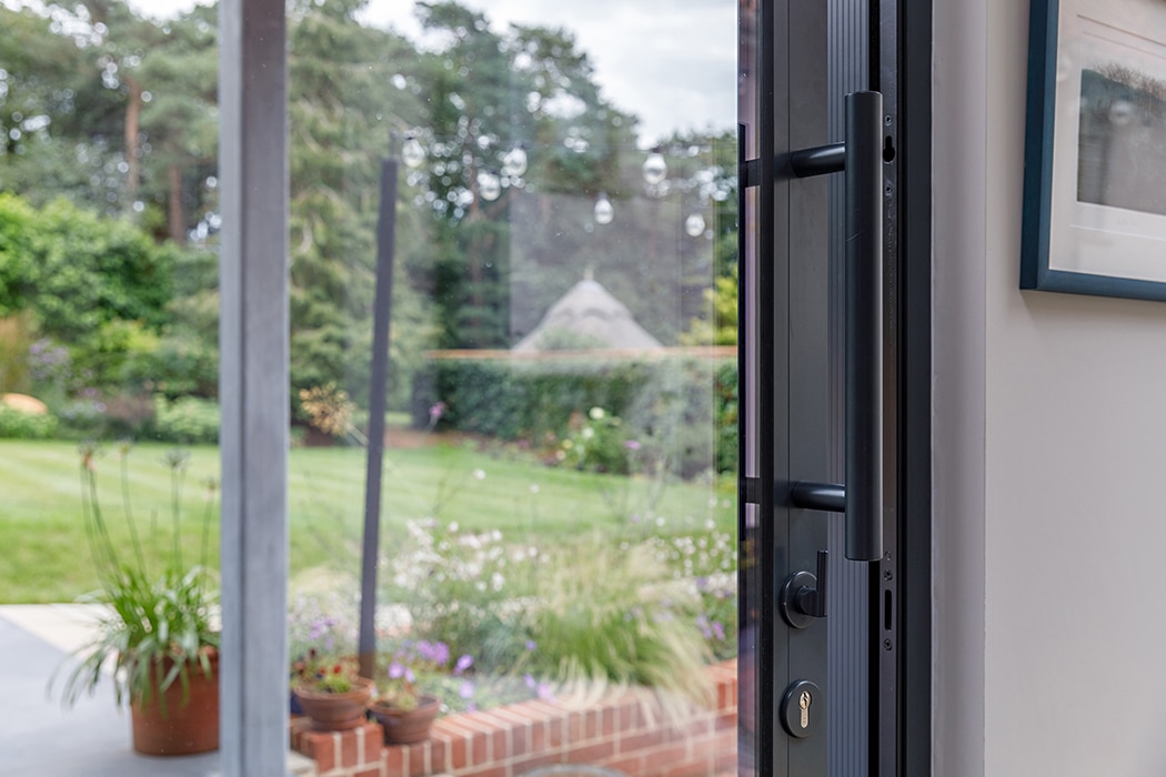 Modern black sliding door system opening onto manicured garden with lawn and planted borders, exemplifying contemporary glazing design.