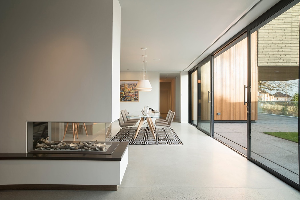 Modern open-plan living space with large sliding glass doors, contemporary dining area, and linear fireplace showcasing thermal efficiency design.